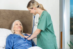 Female caretaker examining senior woman with stethoscope