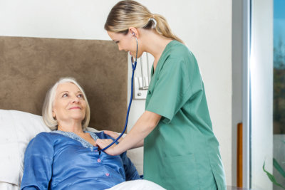 Female caretaker examining senior woman with stethoscope